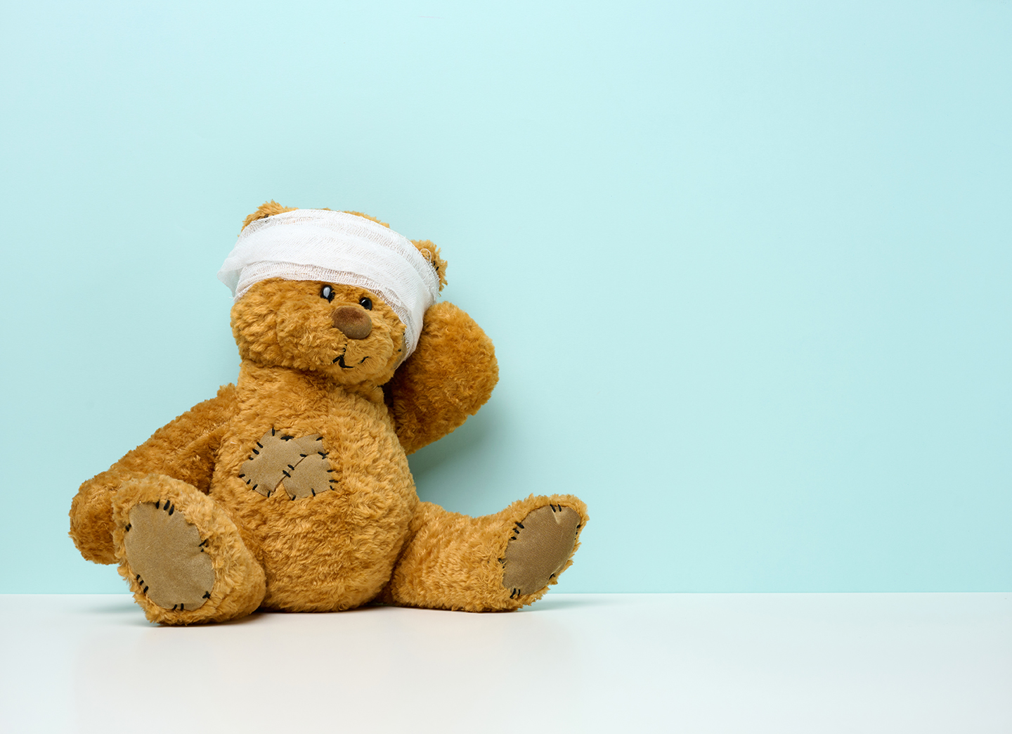 children’s toy teddy bear sits with a bandaged head. Childhood t