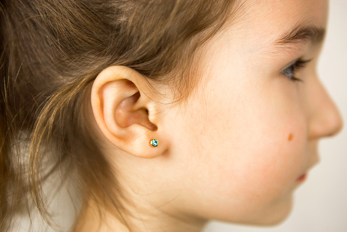 Ear piercing in a child – a girl shows an earring in her ear mad